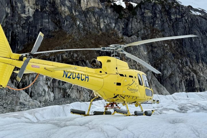 Yellow helicopter landed on a snowy mountain with rocky cliffs in the background.